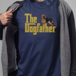 May include: A navy blue t-shirt with a gold glitter design that says "The Dogfather" with a German Shepherd dog standing next to the text.