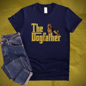 May include: A navy blue t-shirt with a gold glitter design that says "The Dogfather" with a German Shepherd dog standing in front of the text.