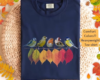 May include: A navy blue t-shirt with a design of five colorful birds perched on a row of autumn leaves. The text "Comfort Colors® Heavyweight Tee-shirt" is printed on the right side of the image.