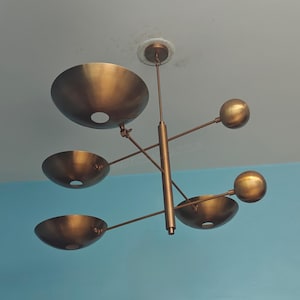 May include: A bronze-colored, mid-century modern style ceiling light fixture. It features three bowl-shaped shades and two spherical accents, all connected by slender rods and a central vertical support. The fixture is mounted on a white ceiling.