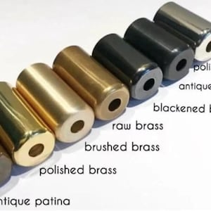 May include: An assortment of cylindrical metal objects in various finishes, including polished chrome, antique black, and brushed brass. The objects are arranged in a row, showcasing different colors and textures. Text labels identify each finish.