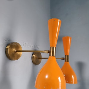 Op de afbeelding: Een paar oranje wandlampen met messing accenten. De lampen hebben een uniek, trompetvormig ontwerp met een gestippeld patroon op de kap.