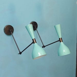 May include: Two aqua-colored wall sconces with a mid-century modern design. Each sconce features a conical shade, a bronze-colored mounting plate, and a black adjustable arm. The sconces are mounted on a light blue wall.