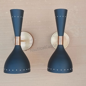 May include: Two black wall sconces with gold accents and a dotted pattern. The sconces are mounted on a beige wall.