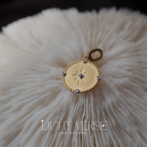 May include: Gold pendant necklace with a star design and small clear stones around the edge. The pendant is on a white coral-like surface.