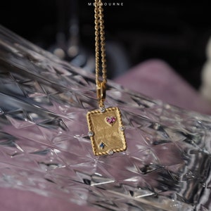 May include: Gold necklace with a rectangular pendant featuring a heart with pink and blue gemstones and the inscription "You are my first love".