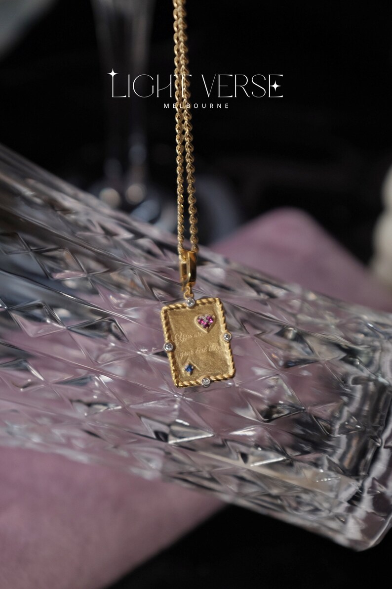 May include: Gold necklace with a rectangular pendant featuring a heart with pink and blue gemstones and the inscription "You are my first love".