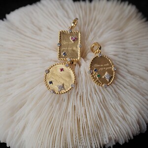 May include: Three gold pendants with colorful gemstones and engraved messages. The pendants are on a white coral background. The messages on the pendants are "You are your best friend", "Here are stars, joy is years", and "Silver and freedom you and forever".