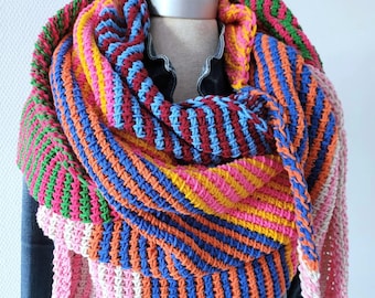 May include: A colorful striped crochet scarf in pink, orange, blue, yellow, and green. The scarf is folded and draped over a mannequin wearing a denim jacket.