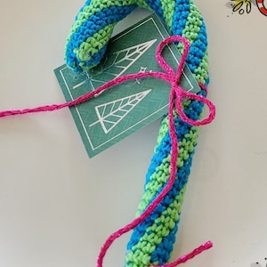 Puede incluir: Un adorno de bastón de caramelo tejido a crochet en rayas verdes y azules con una cinta rosa atada alrededor.