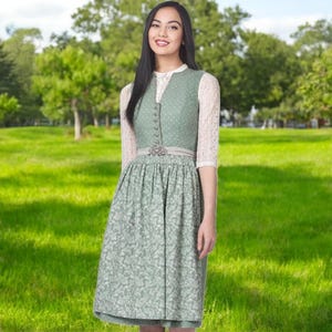 May include: A green dirndl dress with a white blouse and a white lace overlay. The dress has a white belt with a silver buckle and a white polka dot pattern.