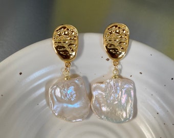 Peut inclure: Une paire de boucles d'oreilles en or avec un dessus ovale texturé et une grosse perle blanche de forme irrégulière qui pend de chaque côté.