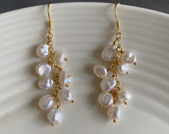 May include: A pair of gold dangle earrings with white pearl drops. The earrings have a delicate chain design and feature multiple pearl drops of varying sizes.