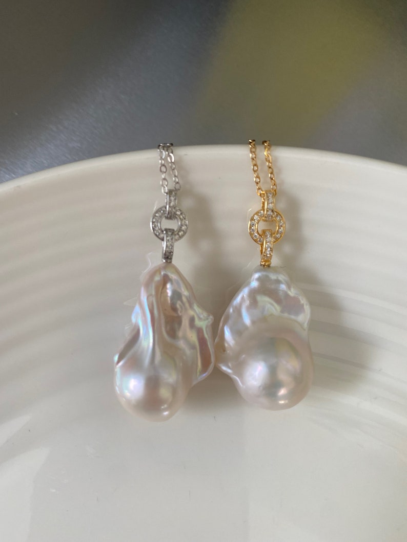 Pu&ograve; includere: Due collane di perle con un ciondolo a forma di perla barocca e un ciondolo circolare tempestato di diamanti. Una collana ha una catena d'argento e l'altra una catena d'oro.