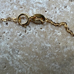 Pu&ograve; includere: Primo piano di una chiusura di collana a catena dorata con un'etichetta che recita "S925".