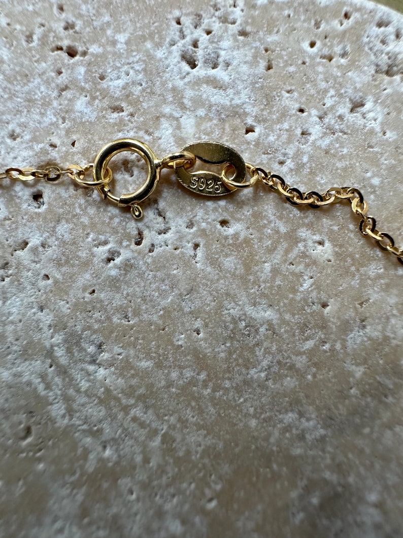 Pu&ograve; includere: Primo piano di una chiusura di collana a catena dorata con un'etichetta che recita "S925".