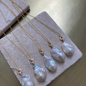 Pu&ograve; includere: Cinque collane d'oro con ciondoli a forma di perla barocca e chiusura tempestata di diamanti. Le perle sono bianche e hanno un'irradiazione iridescente.