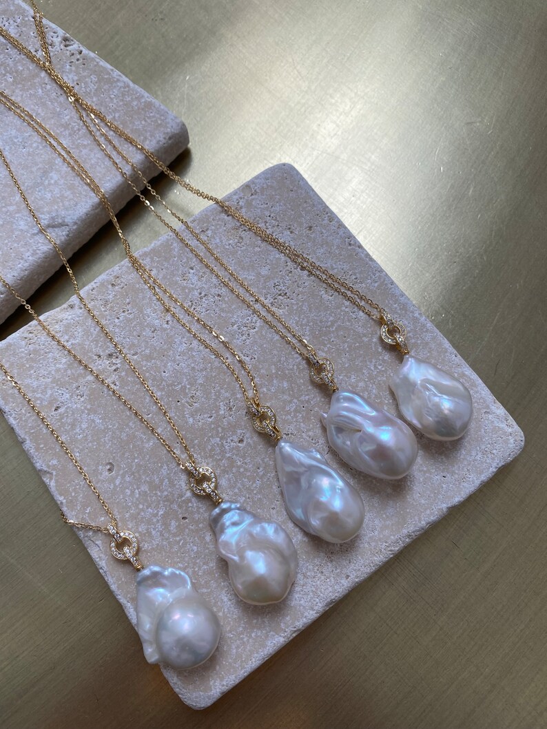 Pu&ograve; includere: Cinque collane d'oro con ciondoli a forma di perla barocca e chiusura tempestata di diamanti. Le perle sono bianche e hanno un'irradiazione iridescente.
