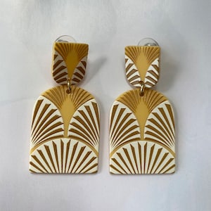 Könnte beinhalten: Ein Paar geometrische Ohrringe mit goldenen und weißen Mustern. Die Ohrringe sind aus einem leichten Material gefertigt und haben ein modernes Design.