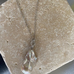 Pu&ograve; includere: Una collana con catena d'argento con un grande ciondolo di perla bianca irregolare.