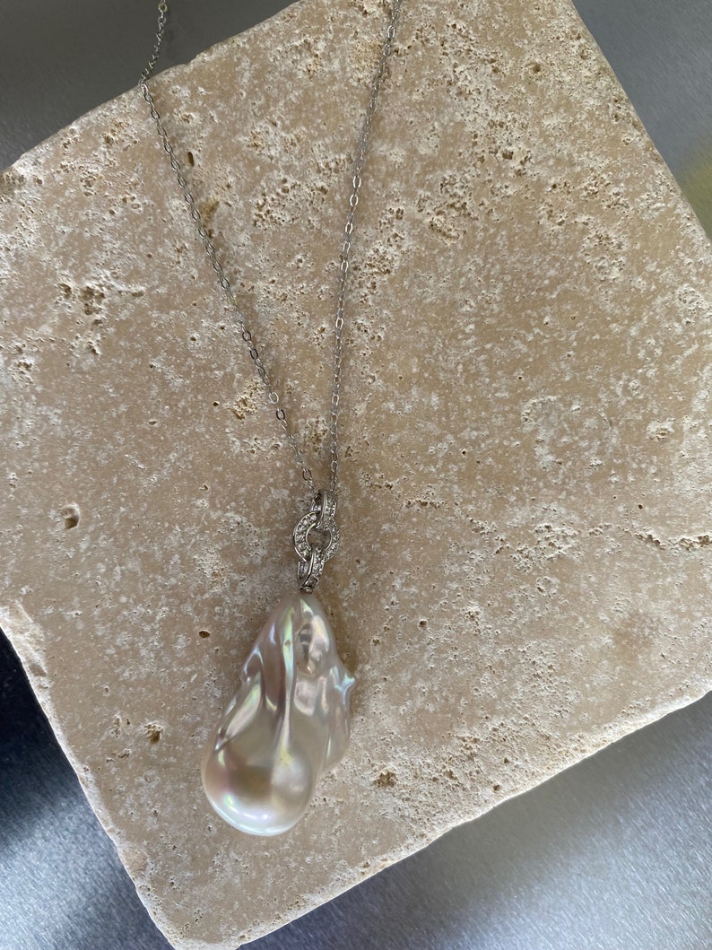 Pu&ograve; includere: Una collana con catena d'argento con un grande ciondolo di perla bianca irregolare.