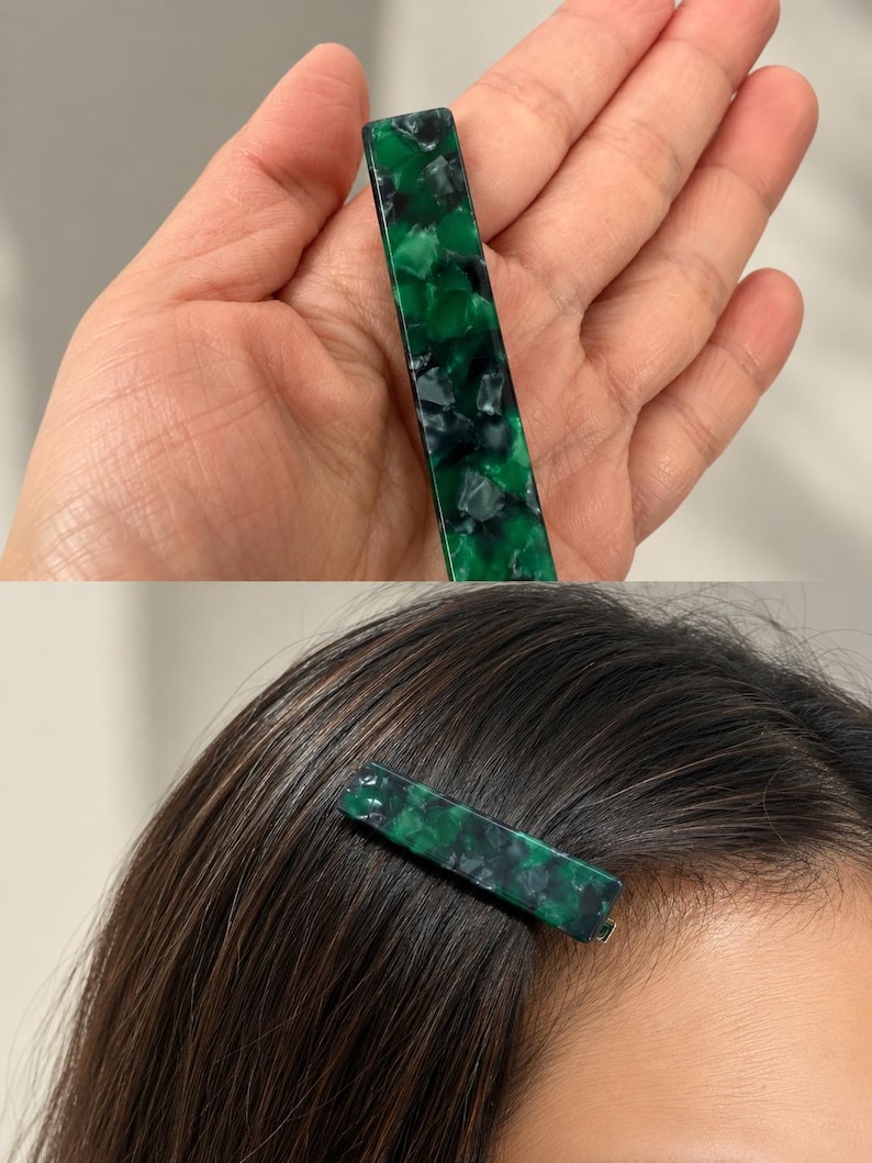 Puede incluir: Una pinza para el pelo rectangular con un patr&oacute;n veteado verde y negro. La pinza se muestra en una mano y tambi&eacute;n en el pelo de una persona. La pinza mide aproximadamente 7,6 cm de largo.