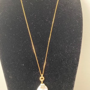 Pu&ograve; includere: Una collana con catena d'oro con un grande ciondolo di perla barocca bianca. La perla &egrave; attaccata alla catena con un piccolo anello d'oro che &egrave; incastonato con piccoli diamanti.