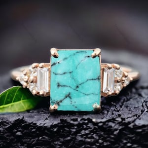 May include: A turquoise gemstone ring with a rectangular cut stone and two smaller accent stones on either side. The ring is set in rose gold.