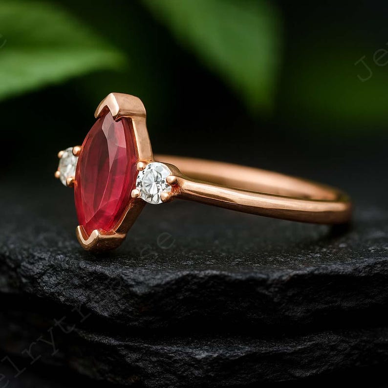 K&ouml;nnte beinhalten: Ros&eacute;goldener Ring mit einem markisenf&ouml;rmigen Rubin-Mittelstein und zwei kleineren runden Diamanten. Band und Fassung des Rings sind ros&eacute;goldfarben, wobei der Rubinstein prominent zur Geltung kommt.