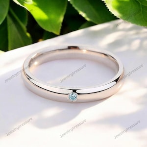 Może przedstawiać: Prosty srebrny pierścionek z małym, jasnoniebieskim kamieniem szlachetnym osadzonym w środku.