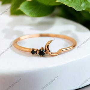 May include: A delicate gold ring with a crescent moon design and three black gemstones. The ring is a minimalist style and would make a great gift.