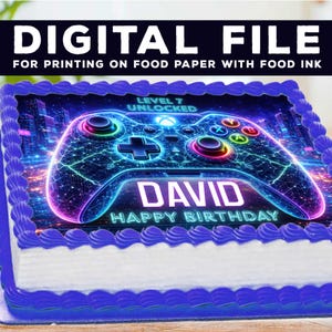 May include: A birthday cake with a blue border and white icing. The cake features a colourful image of a video game controller, the name "DAVID", and the words "HAPPY BIRTHDAY". The text "DIGITAL FILE" is at the top.