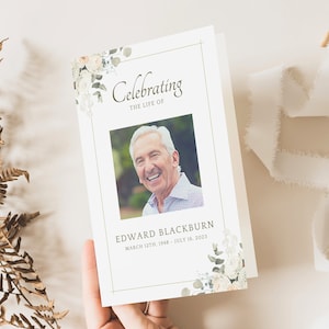 May include: A memorial card featuring a photograph of a smiling older man. The card reads "Celebrating the Life of Edward Blackburn" with dates. Floral accents in white and green frame the photo and text.
