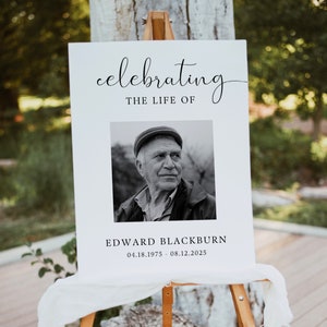 May include: A white sign with black text and a black and white photo of a man. The sign reads "celebrating the life of Edward Blackburn 04.18.1975 - 08.12.2025".