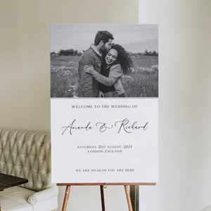 Op de afbeelding: Een zwart-witte huwelijkswelkomstbord met een foto van een stel dat elkaar omhelst. Het bord luidt "Welkom op de bruiloft van Amanda & Richard, zaterdag 21 augustus 2024, Londen, Engeland. We zijn zo blij dat je er bent."