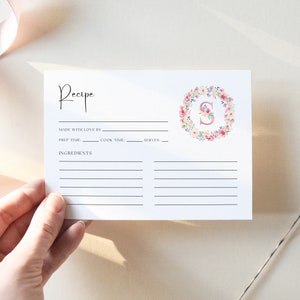 May include: A printable recipe card with a floral wreath design featuring the letter "S" in pink. The card has lines for writing the recipe name, ingredients, prep time, cook time, and servings.