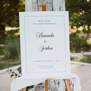 Op de afbeelding: Een wit welkomsbord voor een bruiloft met zwarte tekst. Het bord staat: "Welkom op onze bruiloft Amanda & Jordan Zaterdag 21 augustus 2024 We zijn zo blij dat je er bent."