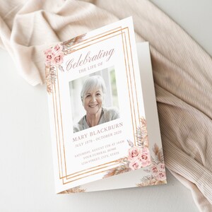 Op de afbeelding: Een witte kaart met een gouden frame en bloemmotieven. De kaart vermeldt "Celebrating the Life of Mary Blackburn July 1978 - October 2020 Saturday, August 5th at 10am Your Funeral Home 1234 Street, City, State".