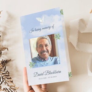 May include: A blue and white memorial card with a photo of a man smiling. The card has a white dove and green leaves on it. The text reads "In loving memory of David Blackburn 03.12.1948 - 07.16.2023".