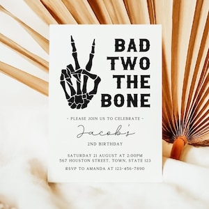 Op de afbeelding: Een zwart-witte uitnodiging met een skelet hand die een vredesteken maakt. De tekst luidt "Bad Two The Bone" en is voor Jacob's 2e verjaardag. De uitnodiging bevat de datum, tijd, adres en RSVP-informatie.