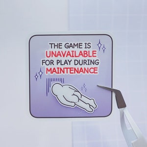May include: A purple sticker with the text "THE GAME IS UNAVAILABLE FOR PLAY DURING MAINTENANCE" in white and red text. A cartoon figure is lying on its back with its arms outstretched. The figure is surrounded by small white stars.