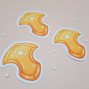 以下が含まれることがあります： 白い輪郭のある黄色とオレンジのステッカーが3つ。各ステッカーは、中央に白い円がある、スタイリッシュな三日月型のデザインが特徴です。