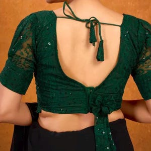 May include: A green sequined and lace blouse with a deep V-neck back and a tie closure. The blouse has short, puffed sleeves.