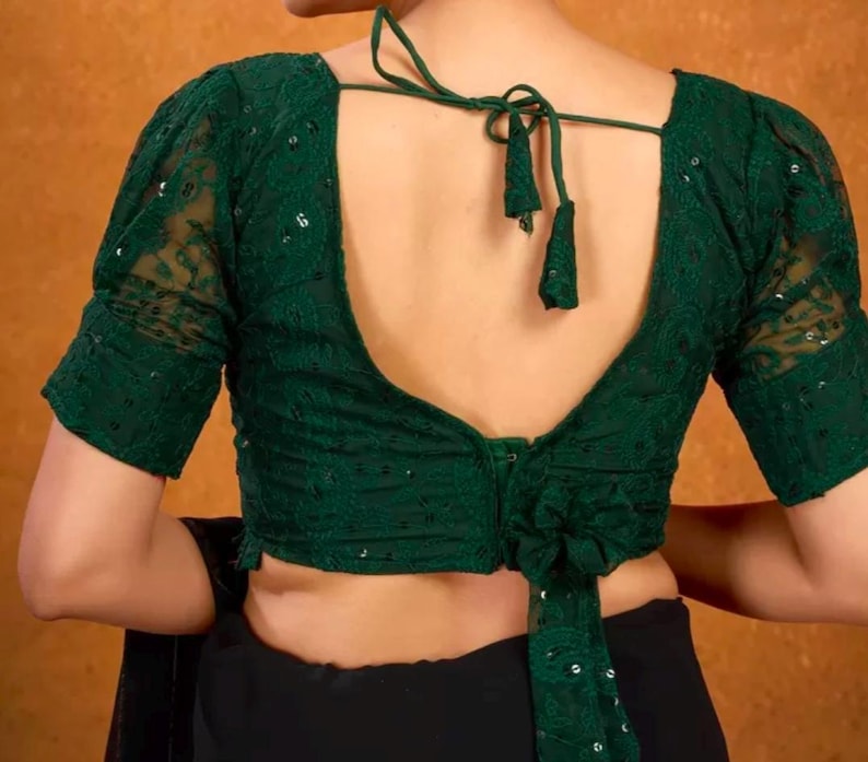 May include: A green sequined and lace blouse with a deep V-neck back and a tie closure. The blouse has short, puffed sleeves.