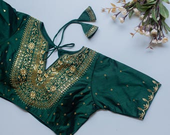 May include: A dark green silk blouse with gold embroidery and sequins. The blouse has a V-neckline and short sleeves. The blouse is decorated with floral patterns.