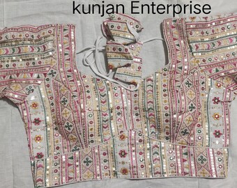 Puede incluir: Blusa blanca bordada con un patrón geométrico y lentejuelas. La blusa tiene cuello redondo y mangas cortas. El texto "kunjan Enterprise" es visible en la parte superior de la imagen.