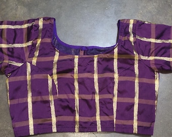 May include: A purple blouse featuring a gold grid pattern throughout the fabric. The garment has a square neckline, short sleeves, and metallic silver trim along the sleeve edges. The design consists of vertical and horizontal gold stripes.