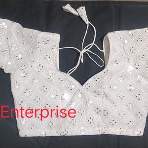 Könnte beinhalten: Weiße bestickte Bluse mit Pailletten und V-Ausschnitt. Die Bluse hat lange Ärmel und einen Bindeverschluss am Rücken. Der Text "kunjan Enterprise" ist am unteren Rand des Bildes sichtbar.