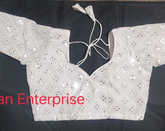 Puede incluir: Blusa blanca bordada con lentejuelas y escote en V. La blusa tiene mangas largas y cierre de lazo en la espalda. El texto "kunjan Enterprise" es visible en la parte inferior de la imagen.