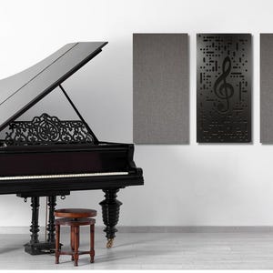 May include: A black grand piano with the lid open, a small wooden stool, and three gray acoustic panels on a white wall. The center panel has a black treble clef cutout.